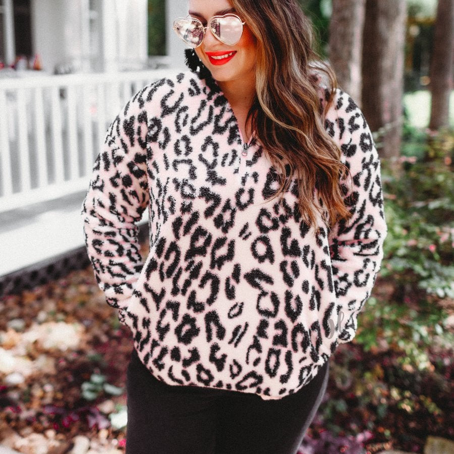 a long-sleeve fluffy pullover with a quarter zip, convenient front pockets, a foldable collar, and an elastic band at the hemline on a pink leopard sherpa fabric