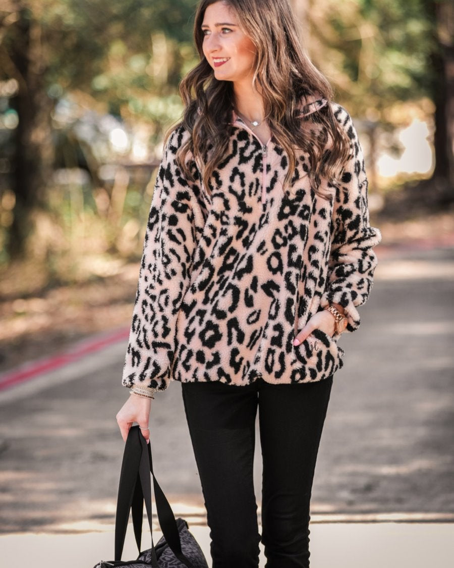a long-sleeve fluffy pullover with a quarter zip, convenient front pockets, a foldable collar, and an elastic band at the hemline on a pink leopard sherpa fabric