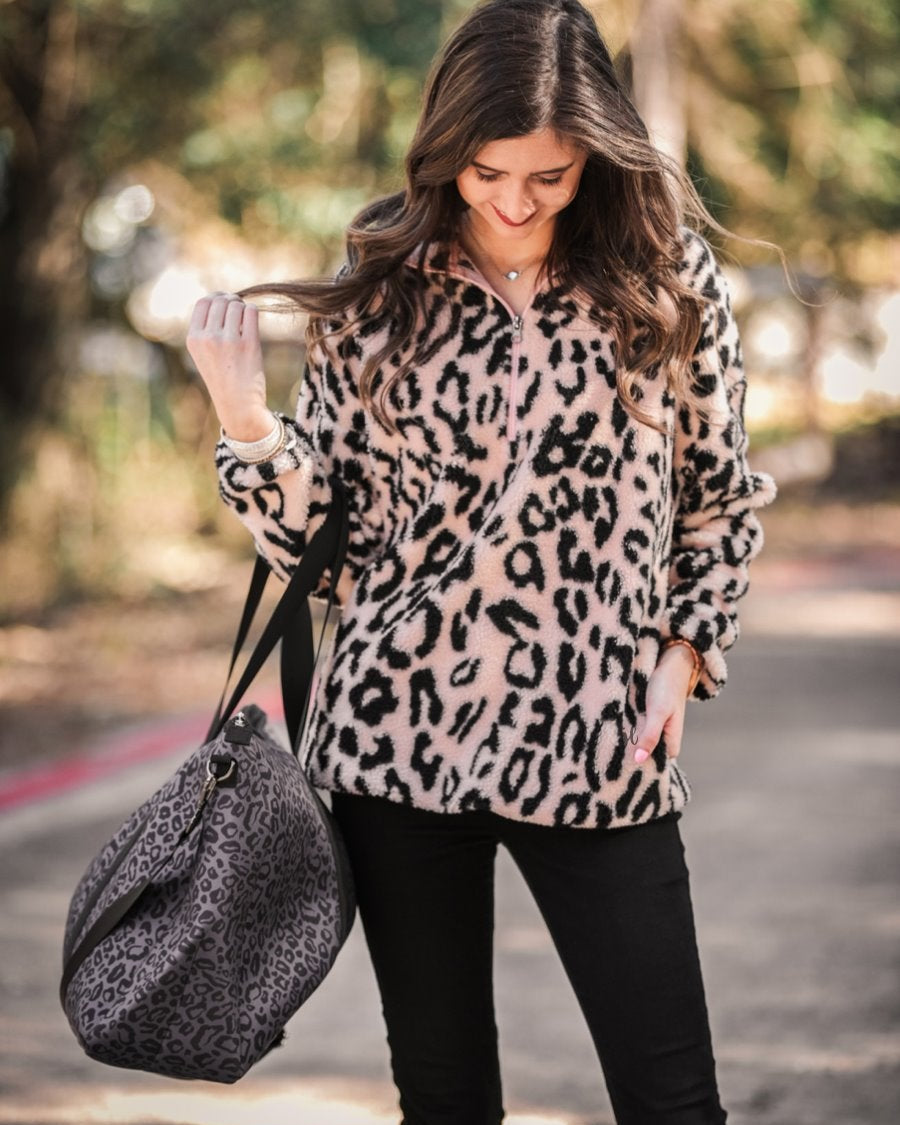a long-sleeve fluffy pullover with a quarter zip, convenient front pockets, a foldable collar, and an elastic band at the hemline on a pink leopard sherpa fabric