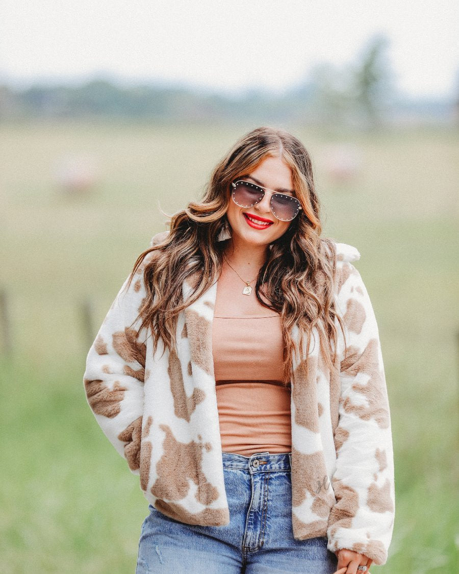 long sleeve open front jacket crafted from a faux fur fabric with a foldable collar and pockets on a cow pattern print and an ivory base