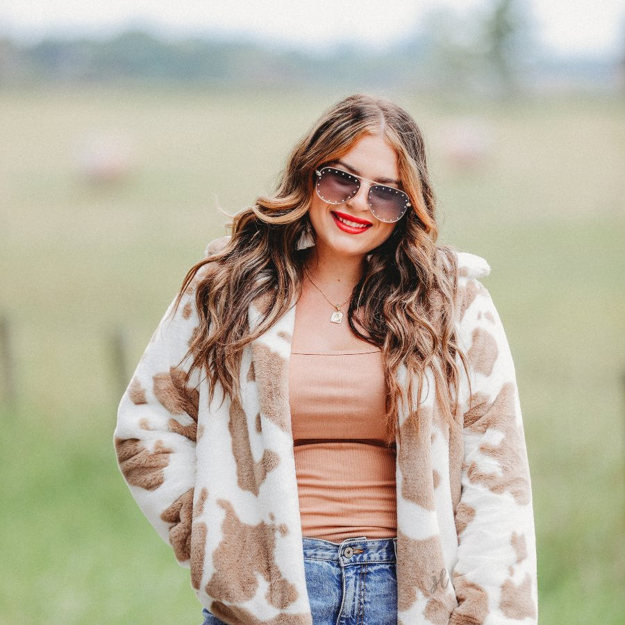 long sleeve open front jacket crafted from a faux fur fabric with a foldable collar and pockets on a cow pattern print and an ivory base
