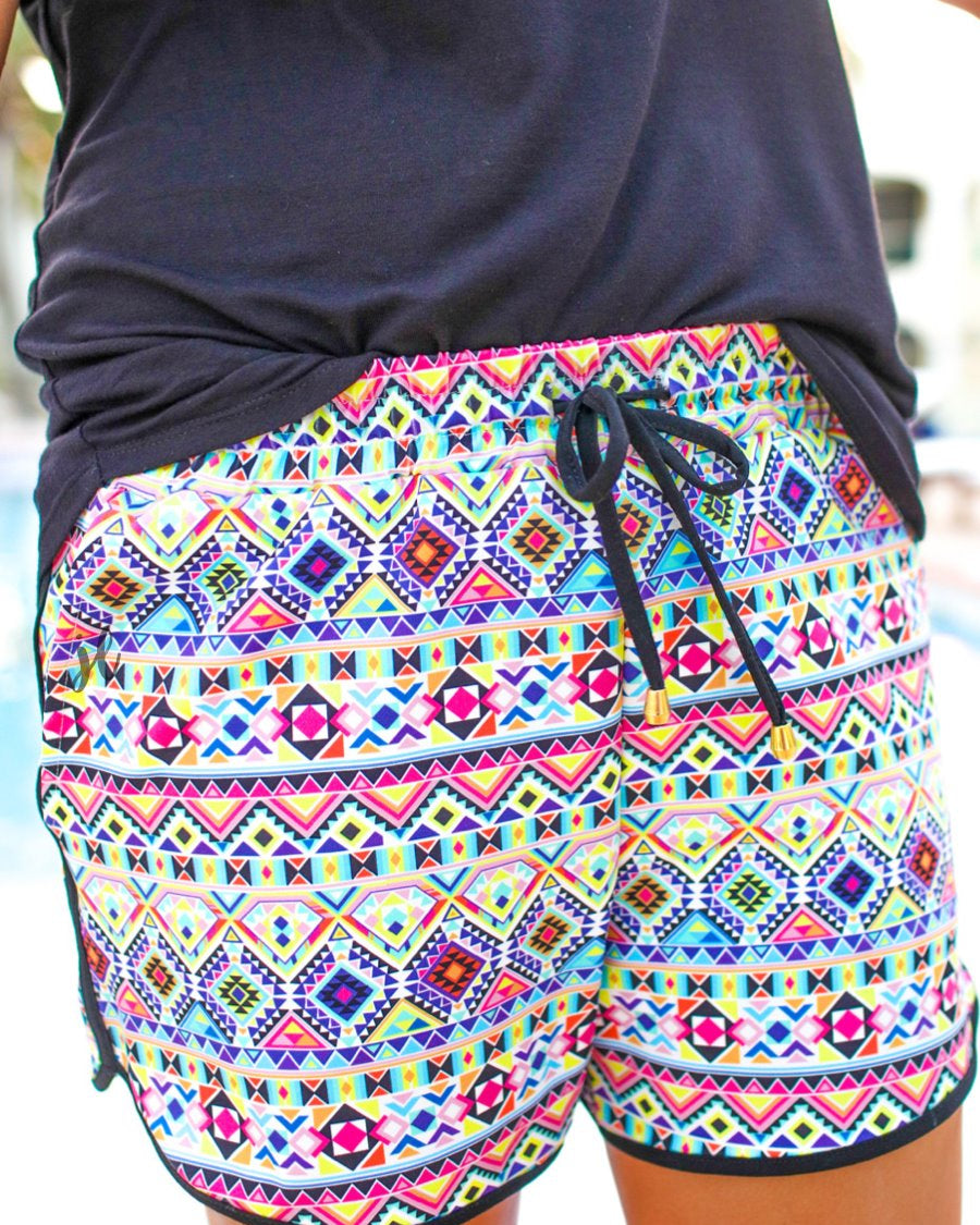 mid-rise relaxed fit activewear shorts with side pockets and a tie waist drawstring with gold bead accents, designed on an Aztec pattern print fabric, ivory base, and black trim