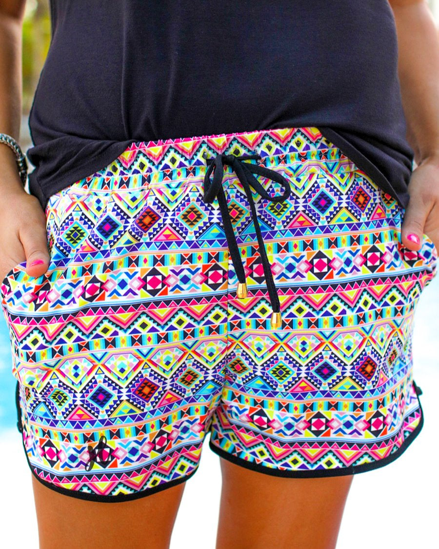 mid-rise relaxed fit activewear shorts with side pockets and a tie waist drawstring with gold bead accents, designed on an Aztec pattern print fabric, ivory base, and black trim