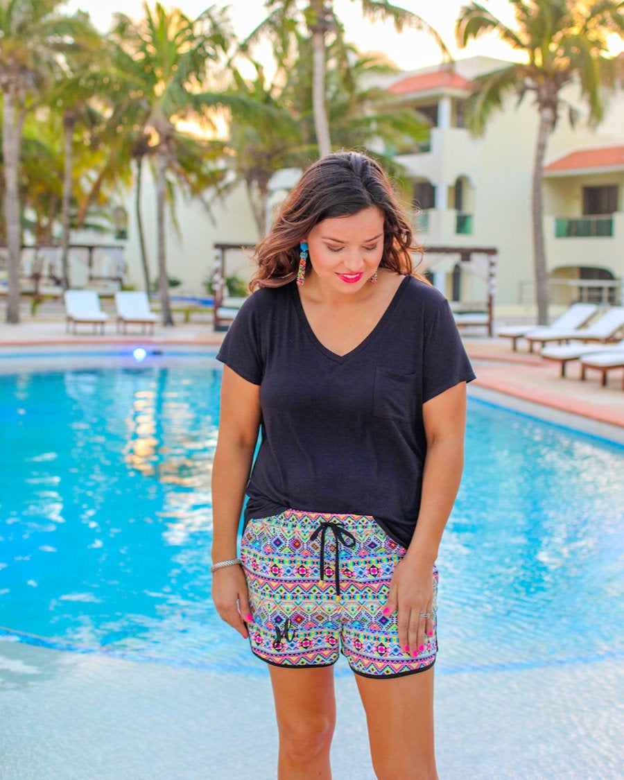 mid-rise relaxed fit activewear shorts with side pockets and a tie waist drawstring with gold bead accents, designed on an Aztec pattern print fabric, ivory base, and black trim