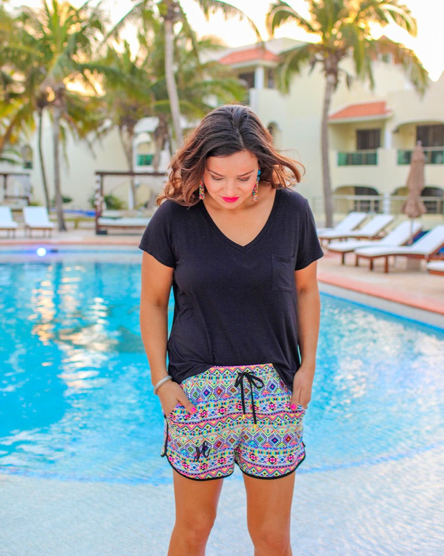 mid-rise relaxed fit activewear shorts with side pockets and a tie waist drawstring with gold bead accents, designed on an Aztec pattern print fabric, ivory base, and black trim