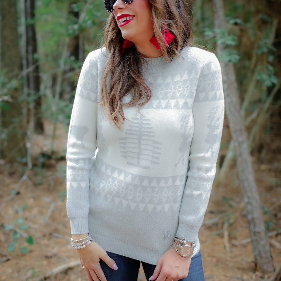 a grey long-sleeve heavy sweater with a ribbed detailing on the neckline, cuffs, and hem on a festive grey and white holiday pattern fabric
