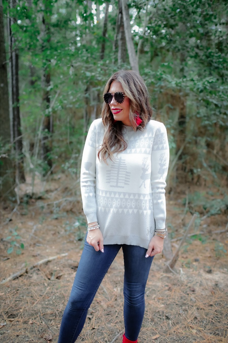 a grey long-sleeve heavy sweater with a ribbed detailing on the neckline, cuffs, and hem on a festive grey and white holiday pattern fabric