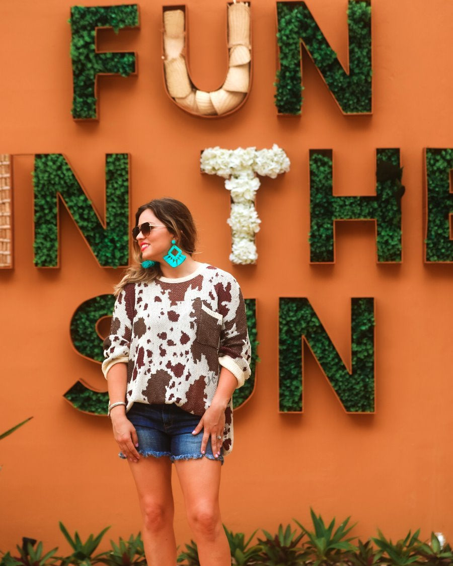 three-quarter cuffed sleeve unlined sweater crafted from a loose knit material with an oversized fit, a rounded neckline, a chest pocket, and trim on the collar, hem, and pocket on a brown cow print and cream base