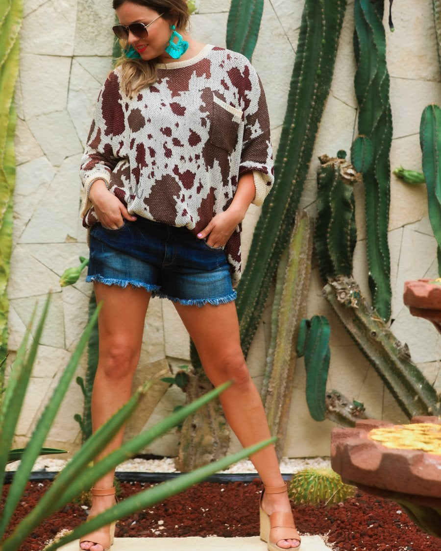 three-quarter cuffed sleeve unlined sweater crafted from a loose knit material with an oversized fit, a rounded neckline, a chest pocket, and trim on the collar, hem, and pocket on a brown cow print and cream base