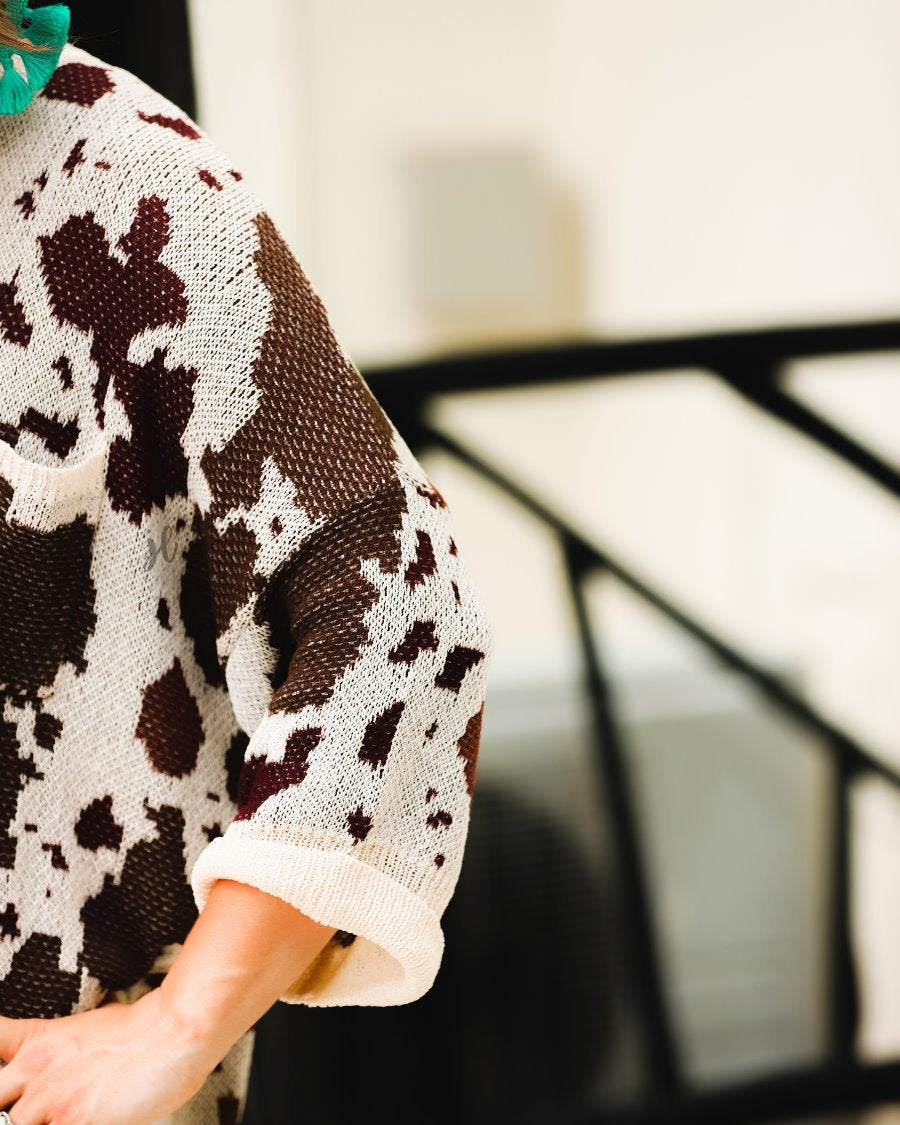 three-quarter cuffed sleeve unlined sweater crafted from a loose knit material with an oversized fit, a rounded neckline, a chest pocket, and trim on the collar, hem, and pocket on a brown cow print and cream base