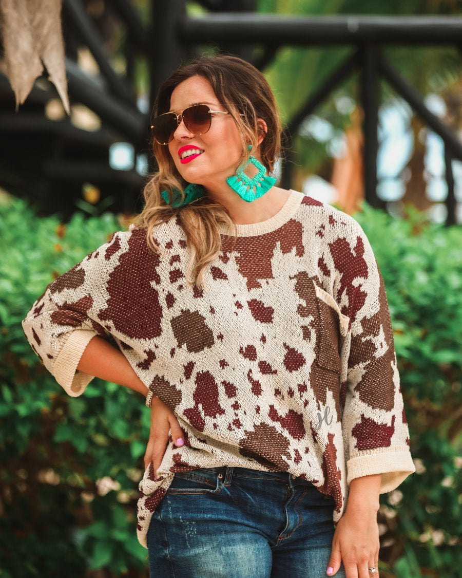 three-quarter cuffed sleeve unlined sweater crafted from a loose knit material with an oversized fit, a rounded neckline, a chest pocket, and trim on the collar, hem, and pocket on a brown cow print and cream base