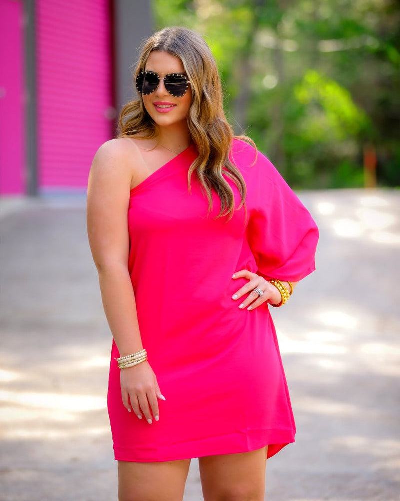 a magenta one-shoulder mini dress with an asymmetrical neckline and a draping, billowy body creating a relaxed silhouette