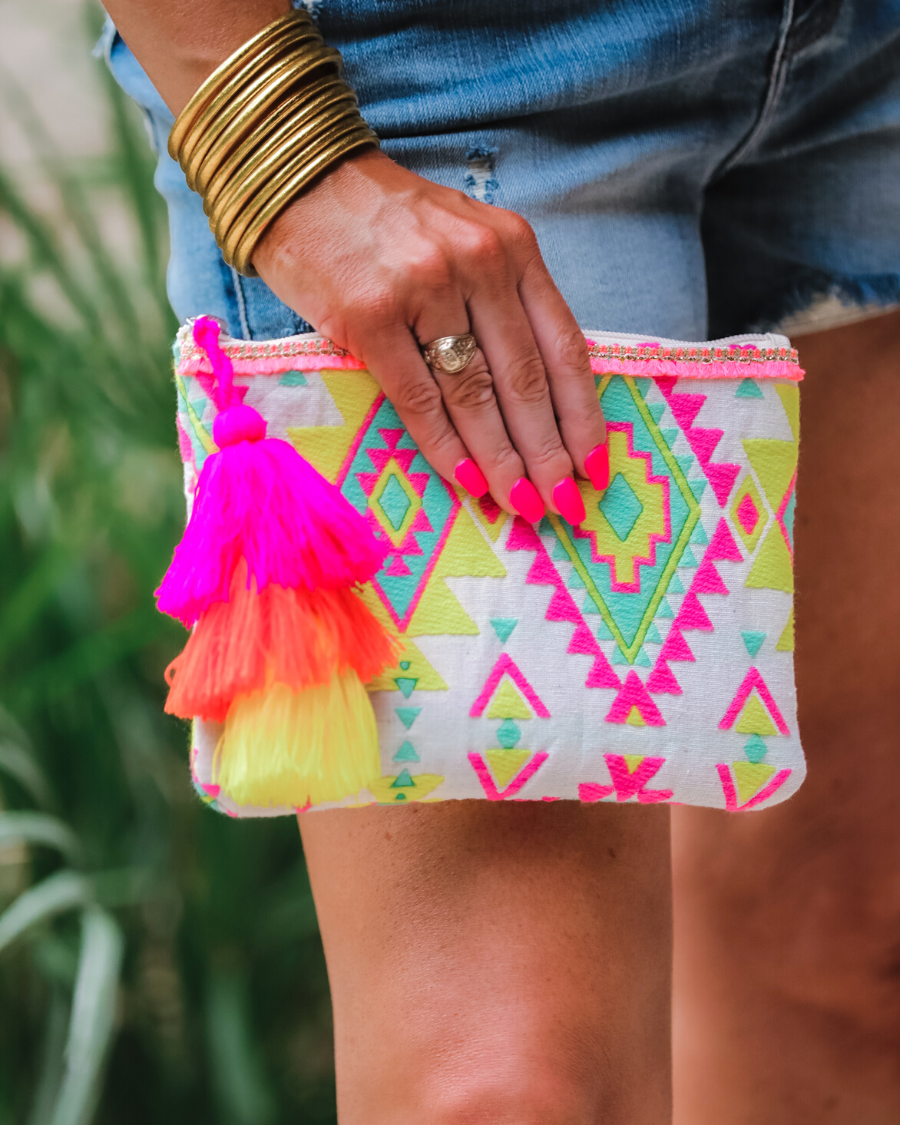 a canvas clutch with a three-tier neon tassel (pink, orange, and yellow) and a silver full zip closure on a geometric and stripe multicolor pattern print