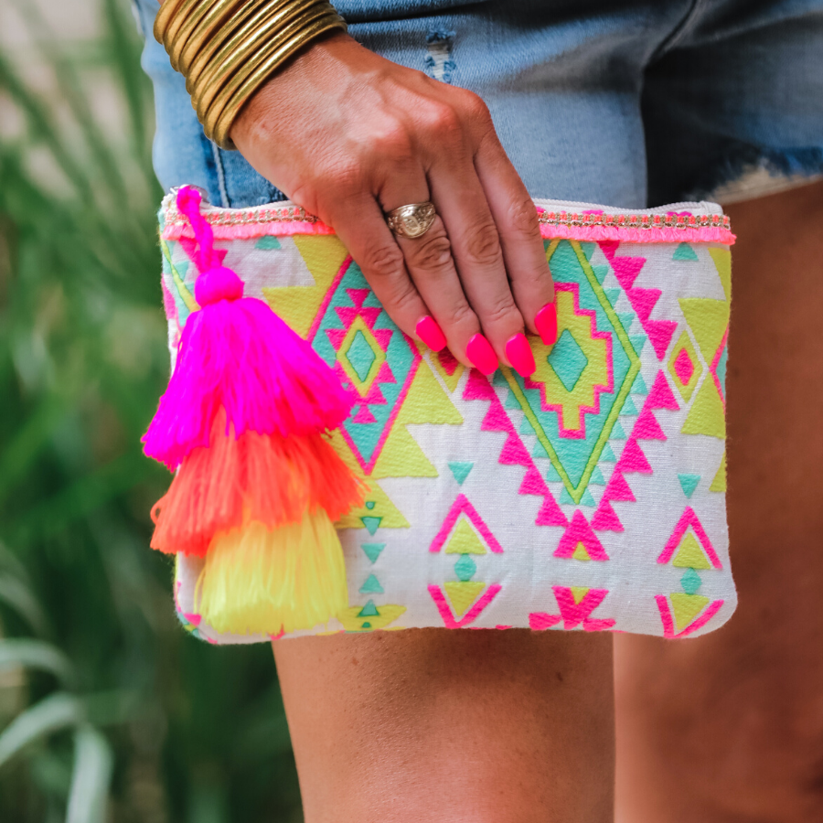 a canvas clutch with a three-tier neon tassel (pink, orange, and yellow) and a silver full zip closure on a geometric and stripe multicolor pattern print