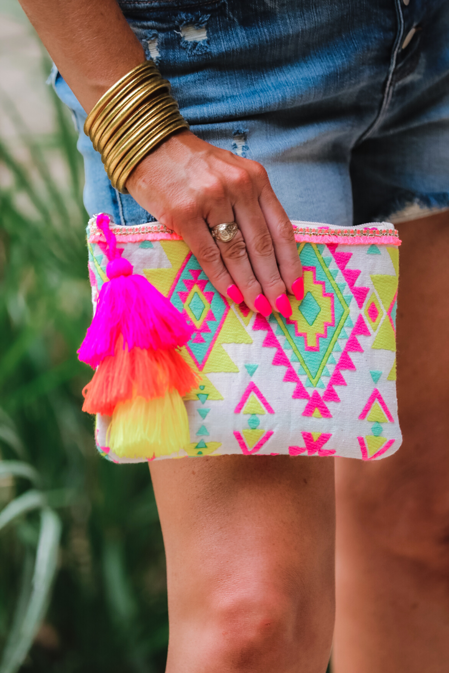 a canvas clutch with a three-tier neon tassel (pink, orange, and yellow) and a silver full zip closure on a geometric and stripe multicolor pattern print