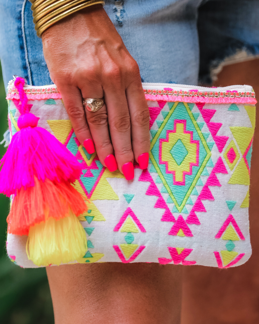 a canvas clutch with a three-tier neon tassel (pink, orange, and yellow) and a silver full zip closure on a geometric and stripe multicolor pattern print