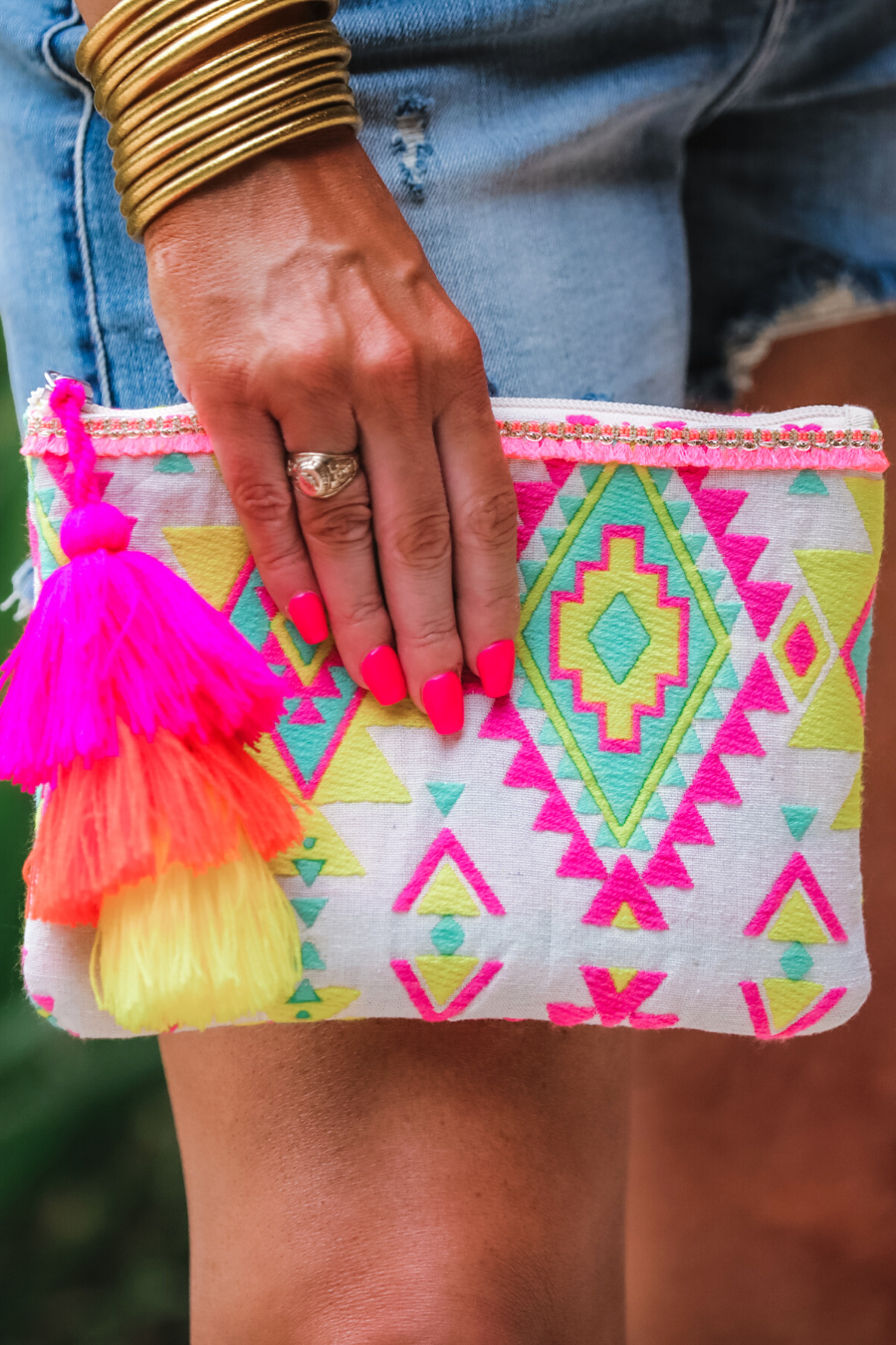 a canvas clutch with a three-tier neon tassel (pink, orange, and yellow) and a silver full zip closure on a geometric and stripe multicolor pattern print