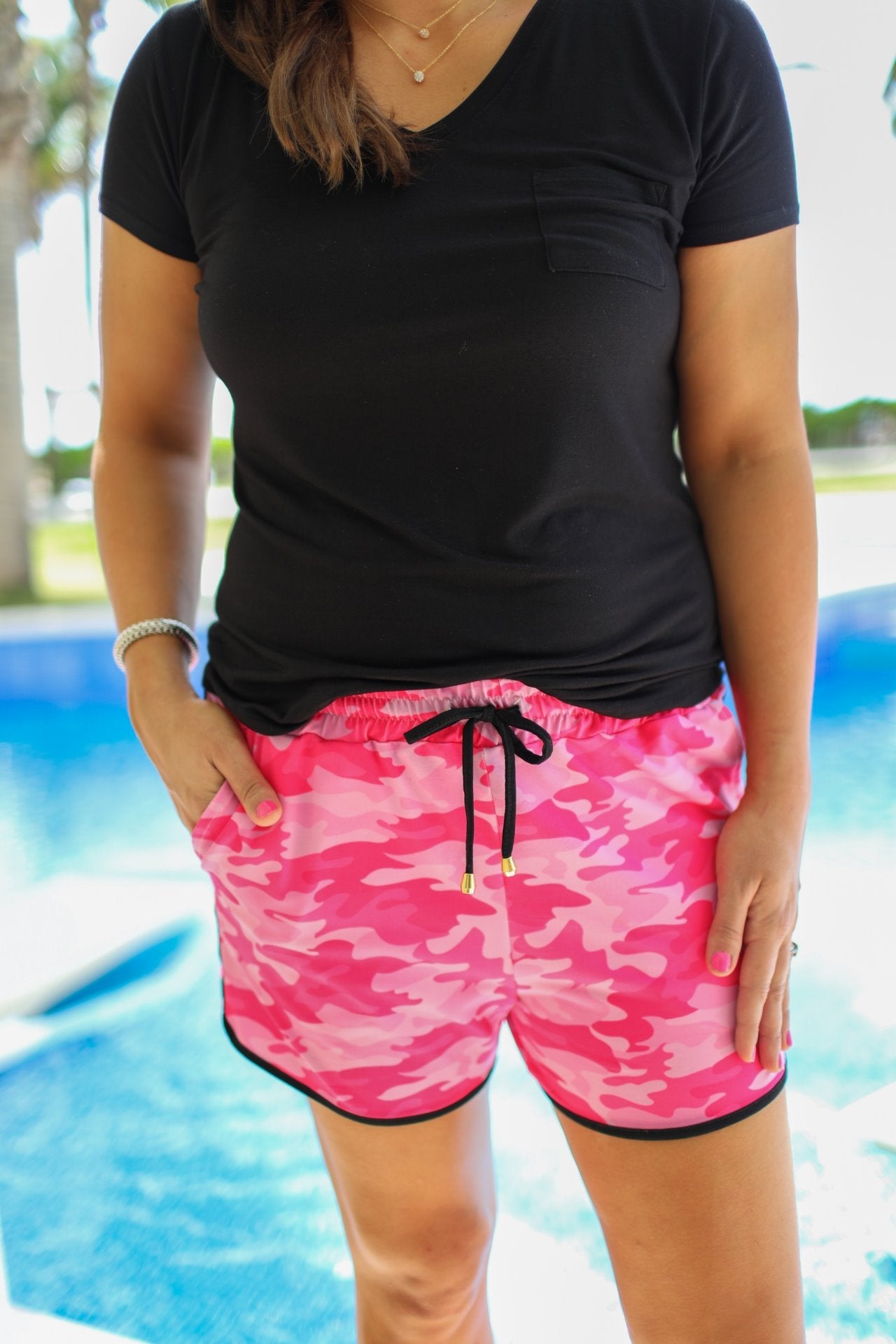 mid-rise relaxed fit activewear shorts with side pockets and a tie waist drawstring with gold bead accents, designed on a pink camo pattern print fabric, pink base, and black trim