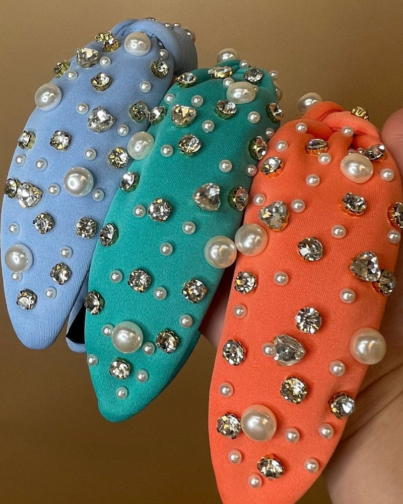 a twisted center knot headband with varying sizes of pearl and rhinestone detailing in blue, coral, and teal