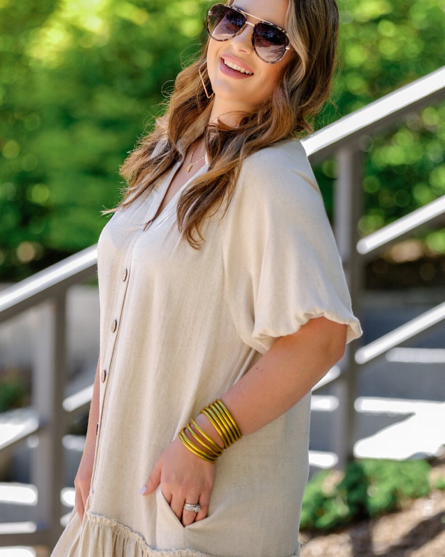 relaxed short-sleeve dress with a V-cut collar, full-button front closure, side pockets, and tiered ruffled hemline in oatmeal