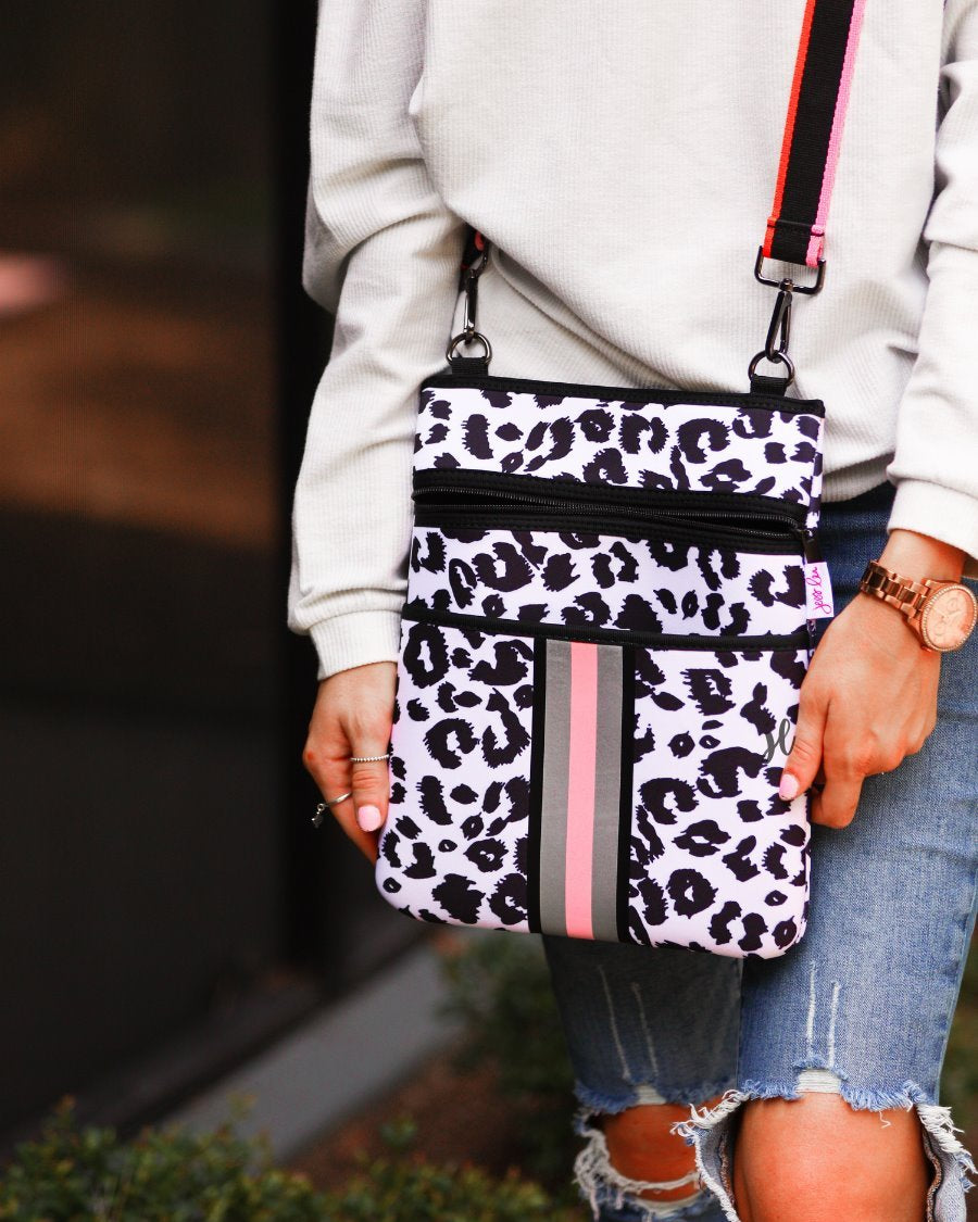 black and white leopard print pattern crossbody bag made of neoprene with an adjustable striped strap (black, orange, and pink), racing stripes (grey and pink), and two front pockets (one zip, one open)