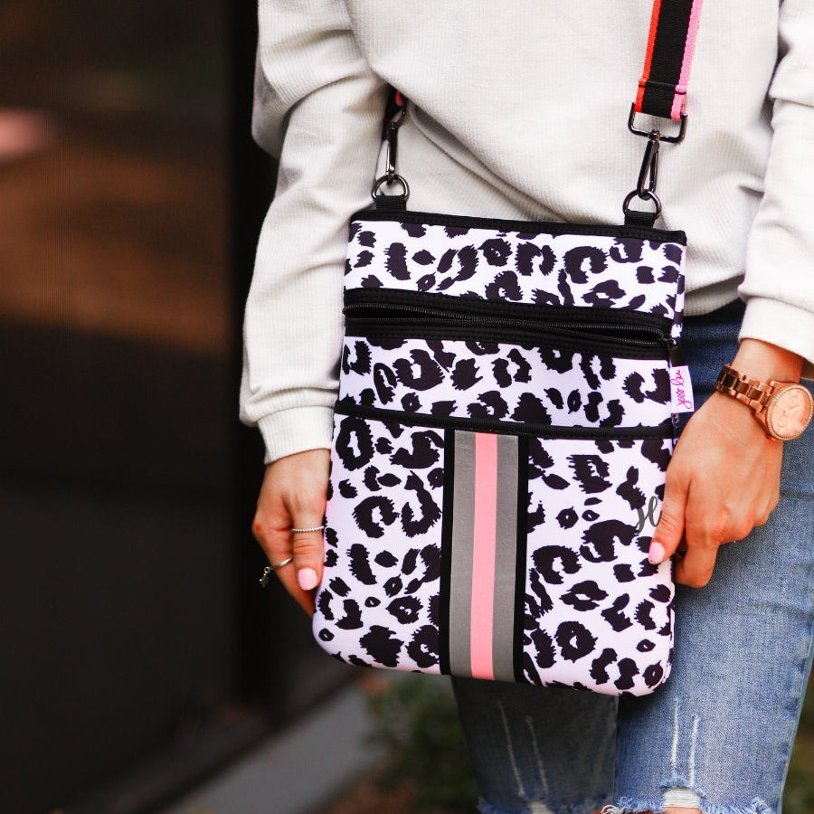 black and white leopard print pattern crossbody bag made of neoprene with an adjustable striped strap (black, orange, and pink), racing stripes (grey and pink), and two front pockets (one zip, one open)
