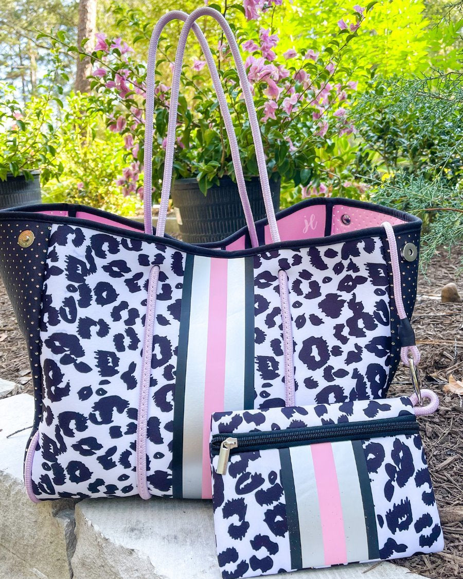 ultra-lightweight tote made of neoprene with a removable hard bottom liner, paracord shoulder straps, removable matching zippered pouch, magnetic side snap closures in silver hardware, black interior (tote and pouch), and racing stripes (black, pink, and white) on a black and pink leopard print pattern
