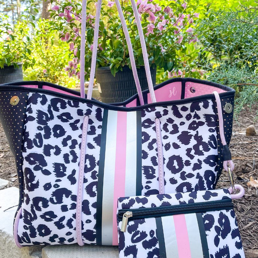 ultra-lightweight tote made of neoprene with a removable hard bottom liner, paracord shoulder straps, removable matching zippered pouch, magnetic side snap closures in silver hardware, black interior (tote and pouch), and racing stripes (black, pink, and white) on a black and pink leopard print pattern