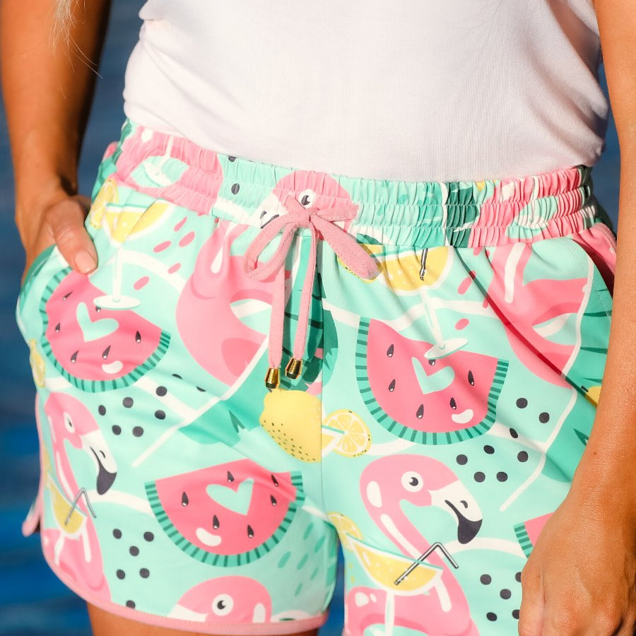 mid-rise relaxed fit activewear shorts with side pockets and a tie waist drawstring with gold bead accents, designed on a playful pool floaties patterned print fabric, mint base, and mauve trim