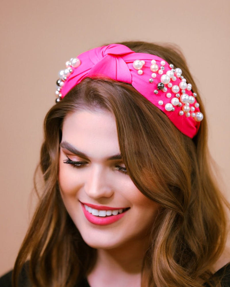 a twisted center knot headband with varying sizes of pearl detailing in pink