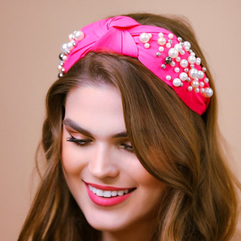 a twisted center knot headband with varying sizes of pearl detailing in pink