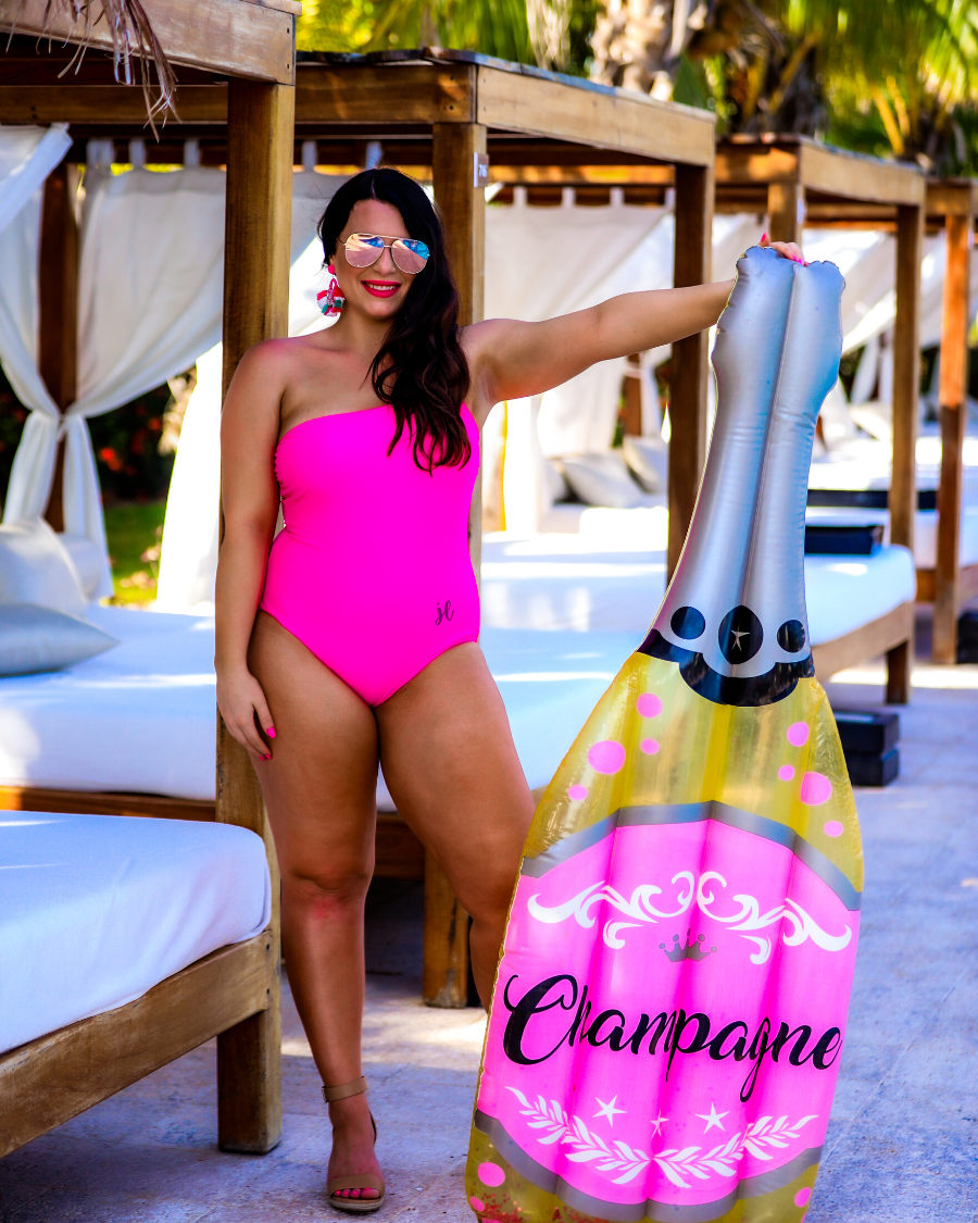 solid pink one-piece swimsuit with a one-shoulder neckline, gold ring detailing on chest, and removable padding