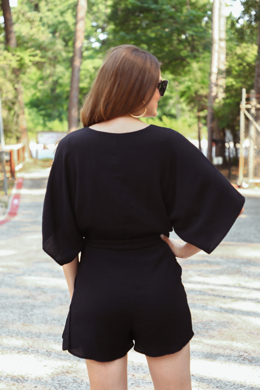 a black lined romper made of soft lightweight fabric with a surplice V-neckline, snap closure, relaxed flowy sleeves, waist-defining accent tie, side pockets, and a flattering easy-to-wear silhouette