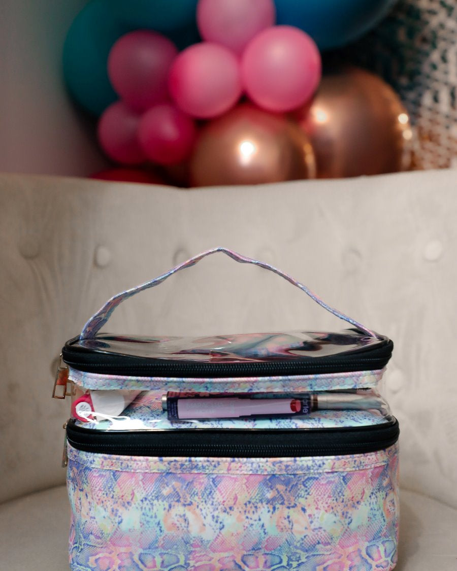 two-tier design with a clear compartment, four brush slots with an elastic band on the inside lid of the main compartment, and a grab-and-go handle with dual gold zippers in a soft pastel snakeskin print