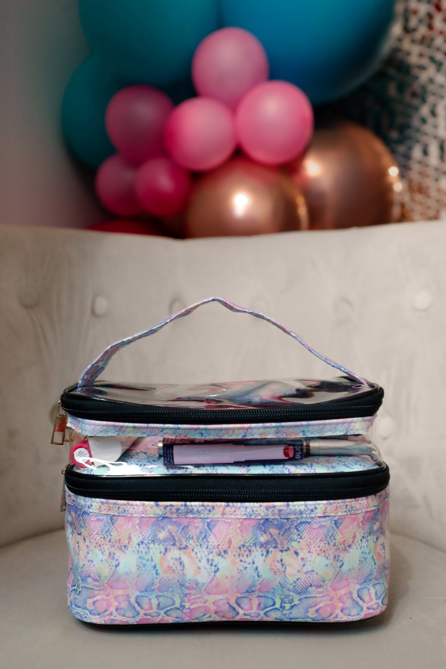 two-tier design with a clear compartment, four brush slots with an elastic band on the inside lid of the main compartment, and a grab-and-go handle with dual gold zippers in a soft pastel snakeskin print