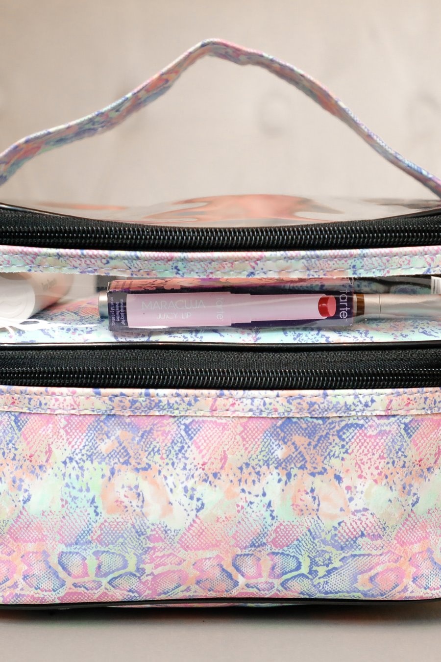 two-tier design with a clear compartment, four brush slots with an elastic band on the inside lid of the main compartment, and a grab-and-go handle with dual gold zippers in a soft pastel snakeskin print