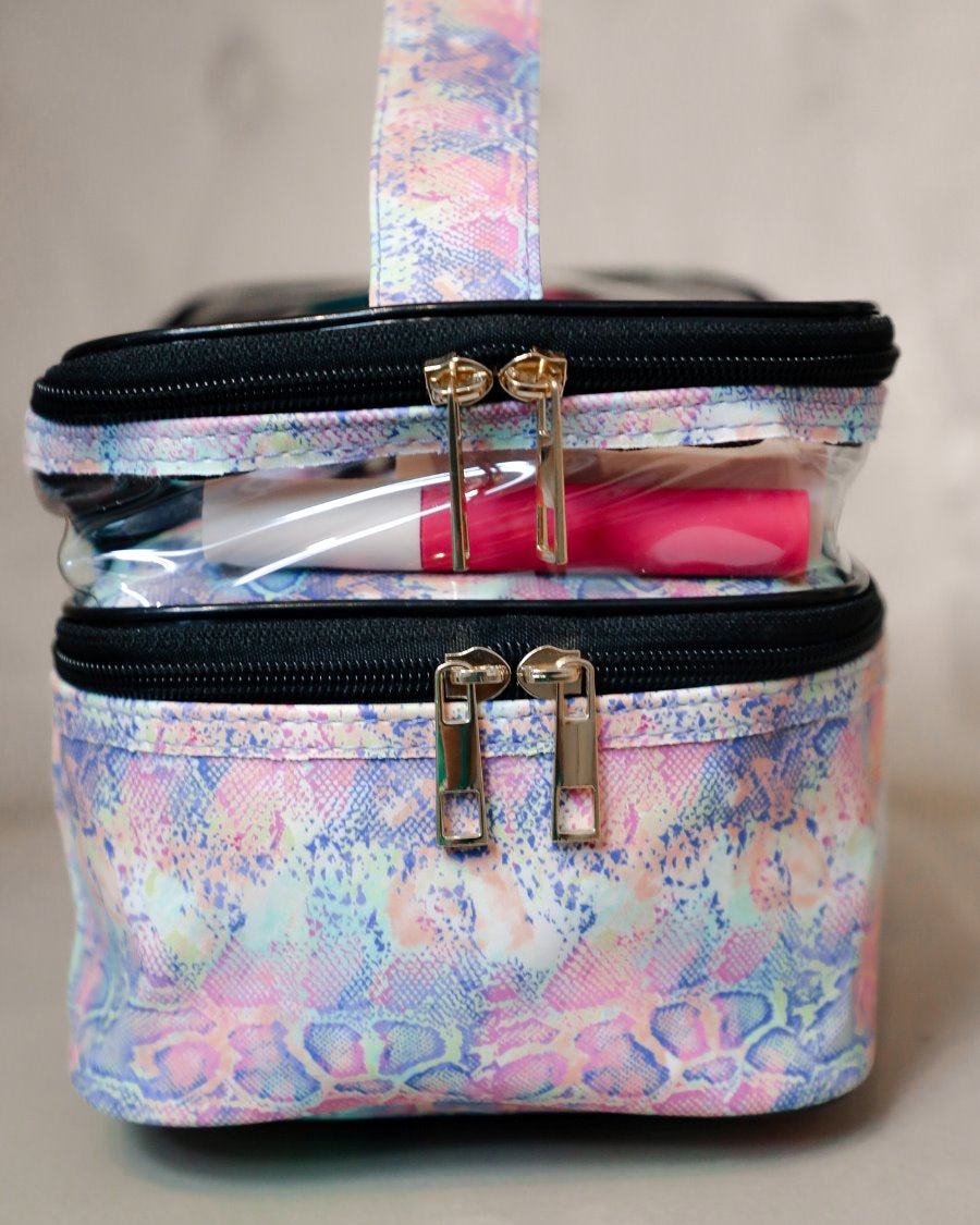 two-tier design with a clear compartment, four brush slots with an elastic band on the inside lid of the main compartment, and a grab-and-go handle with dual gold zippers in a soft pastel snakeskin print