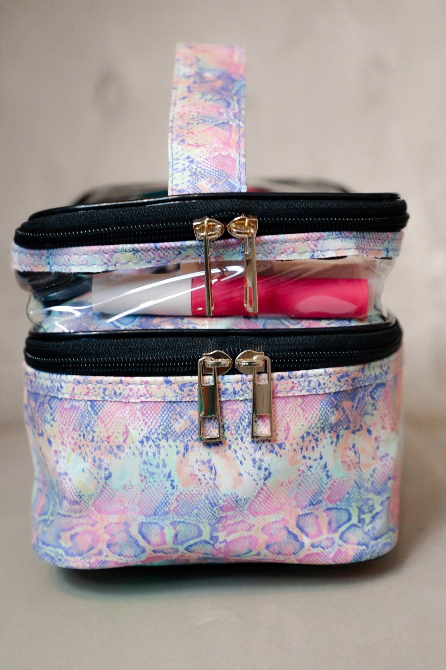 two-tier design with a clear compartment, four brush slots with an elastic band on the inside lid of the main compartment, and a grab-and-go handle with dual gold zippers in a soft pastel snakeskin print
