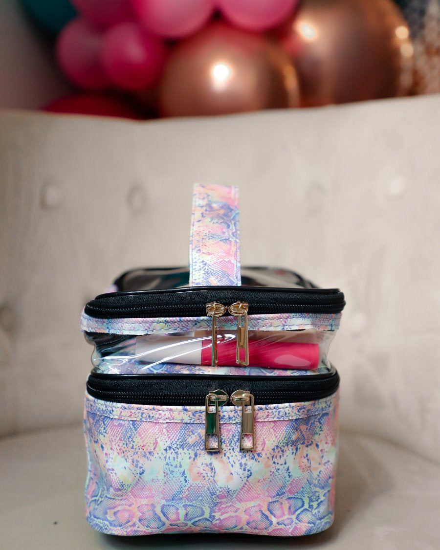 two-tier design with a clear compartment, four brush slots with an elastic band on the inside lid of the main compartment, and a grab-and-go handle with dual gold zippers in a soft pastel snakeskin print
