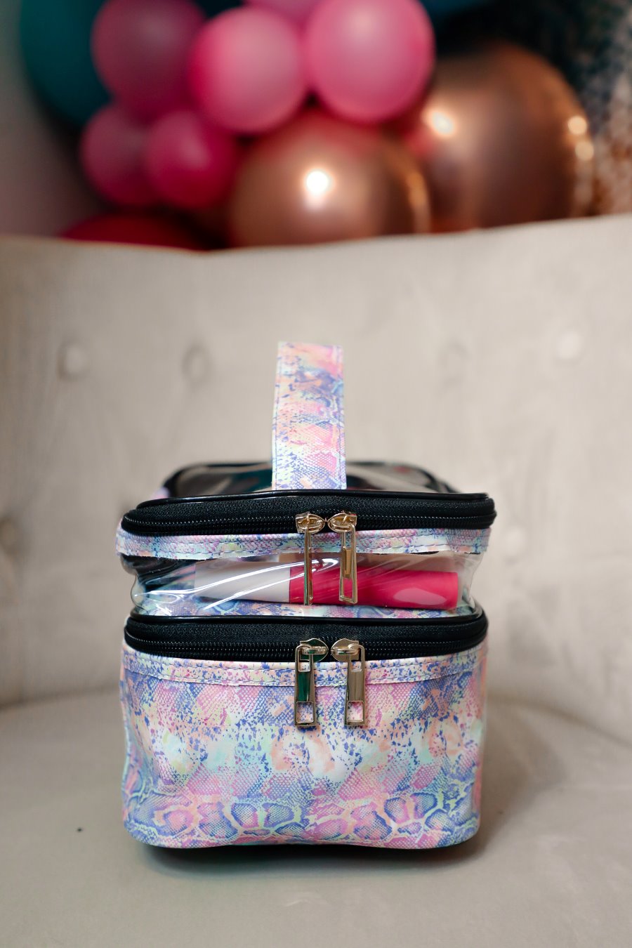 two-tier design with a clear compartment, four brush slots with an elastic band on the inside lid of the main compartment, and a grab-and-go handle with dual gold zippers in a soft pastel snakeskin print