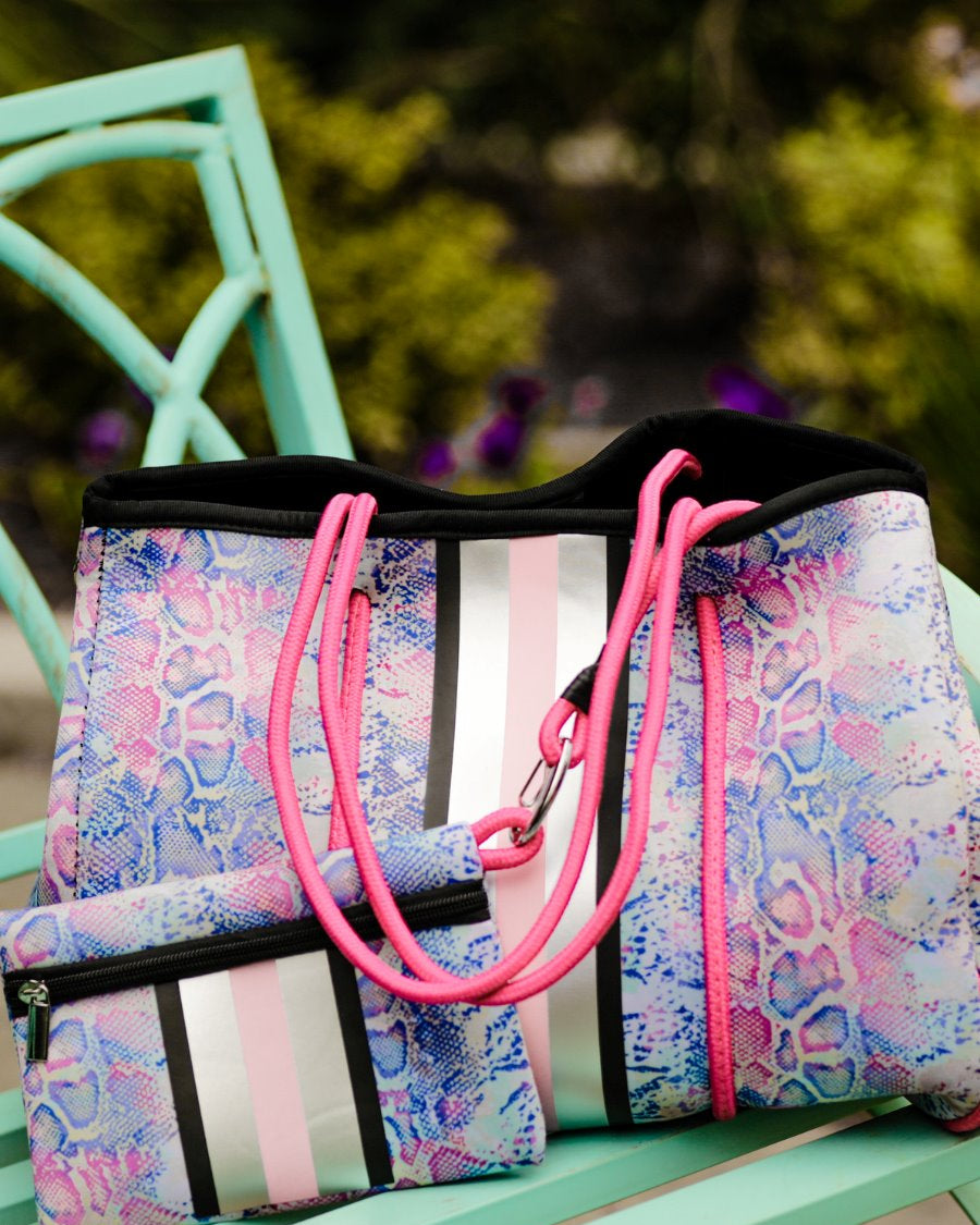 ultra-lightweight tote made of neoprene with a removable hard bottom liner, paracord shoulder straps, removable matching zippered pouch, magnetic side snap closures in silver hardware, black interior (tote and pouch), and racing stripes (black, gray, and pink) on a soft pastel snakeskin pattern