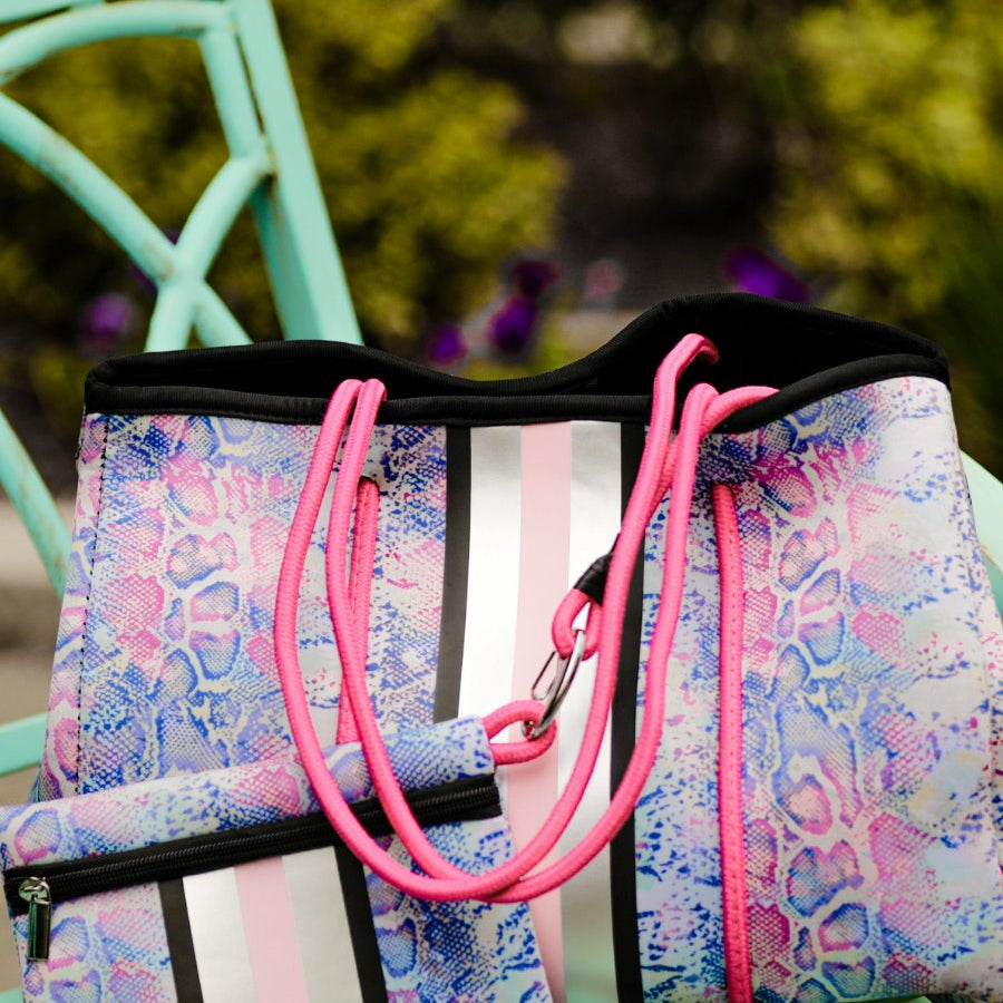 ultra-lightweight tote made of neoprene with a removable hard bottom liner, paracord shoulder straps, removable matching zippered pouch, magnetic side snap closures in silver hardware, black interior (tote and pouch), and racing stripes (black, gray, and pink) on a soft pastel snakeskin pattern