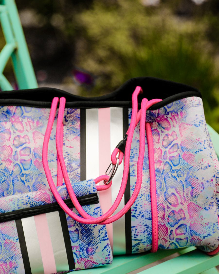 ultra-lightweight tote made of neoprene with a removable hard bottom liner, paracord shoulder straps, removable matching zippered pouch, magnetic side snap closures in silver hardware, black interior (tote and pouch), and racing stripes (black, gray, and pink) on a soft pastel snakeskin pattern