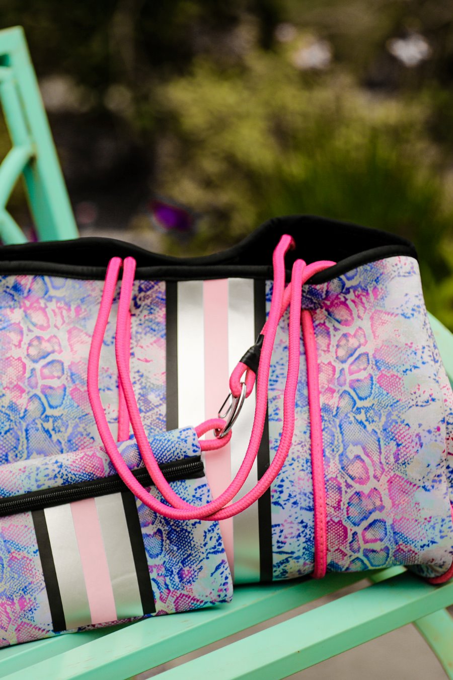 ultra-lightweight tote made of neoprene with a removable hard bottom liner, paracord shoulder straps, removable matching zippered pouch, magnetic side snap closures in silver hardware, black interior (tote and pouch), and racing stripes (black, gray, and pink) on a soft pastel snakeskin pattern