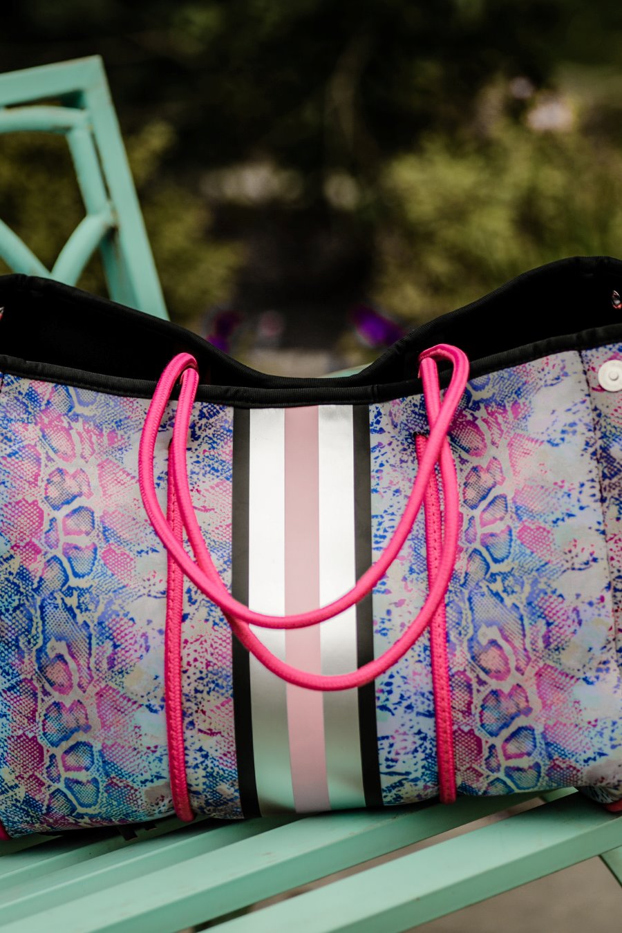 ultra-lightweight tote made of neoprene with a removable hard bottom liner, paracord shoulder straps, removable matching zippered pouch, magnetic side snap closures in silver hardware, black interior (tote and pouch), and racing stripes (black, gray, and pink) on a soft pastel snakeskin pattern
