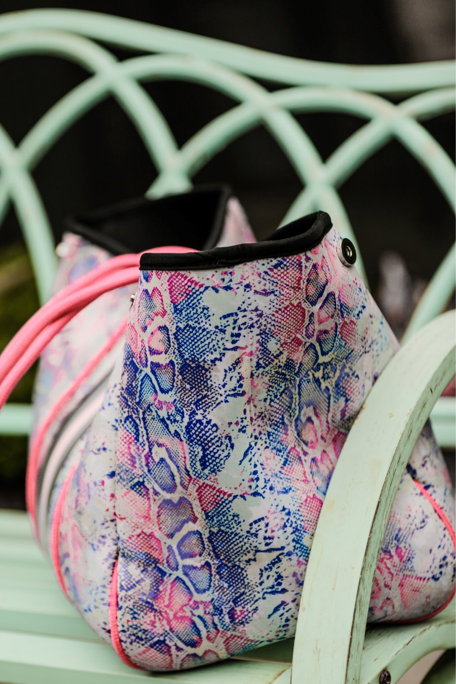 ultra-lightweight tote made of neoprene with a removable hard bottom liner, paracord shoulder straps, removable matching zippered pouch, magnetic side snap closures in silver hardware, black interior (tote and pouch), and racing stripes (black, gray, and pink) on a soft pastel snakeskin pattern