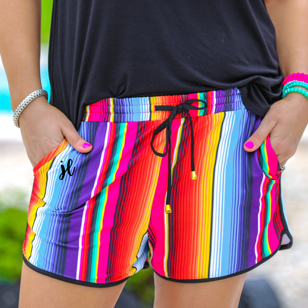 mid-rise relaxed fit activewear shorts with side pockets and a tie waist drawstring with gold bead accents, designed on a multicolor serape pattern print fabric and black trim