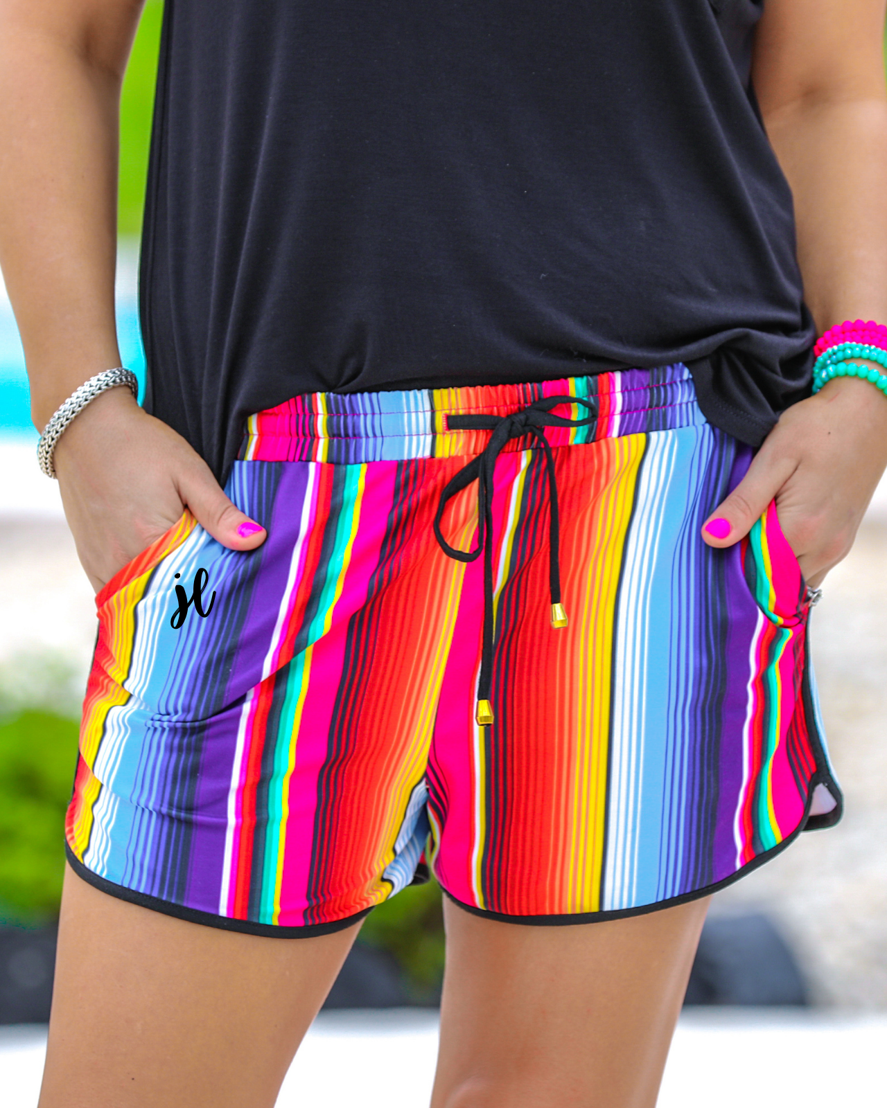 mid-rise relaxed fit activewear shorts with side pockets and a tie waist drawstring with gold bead accents, designed on a multicolor serape pattern print fabric and black trim
