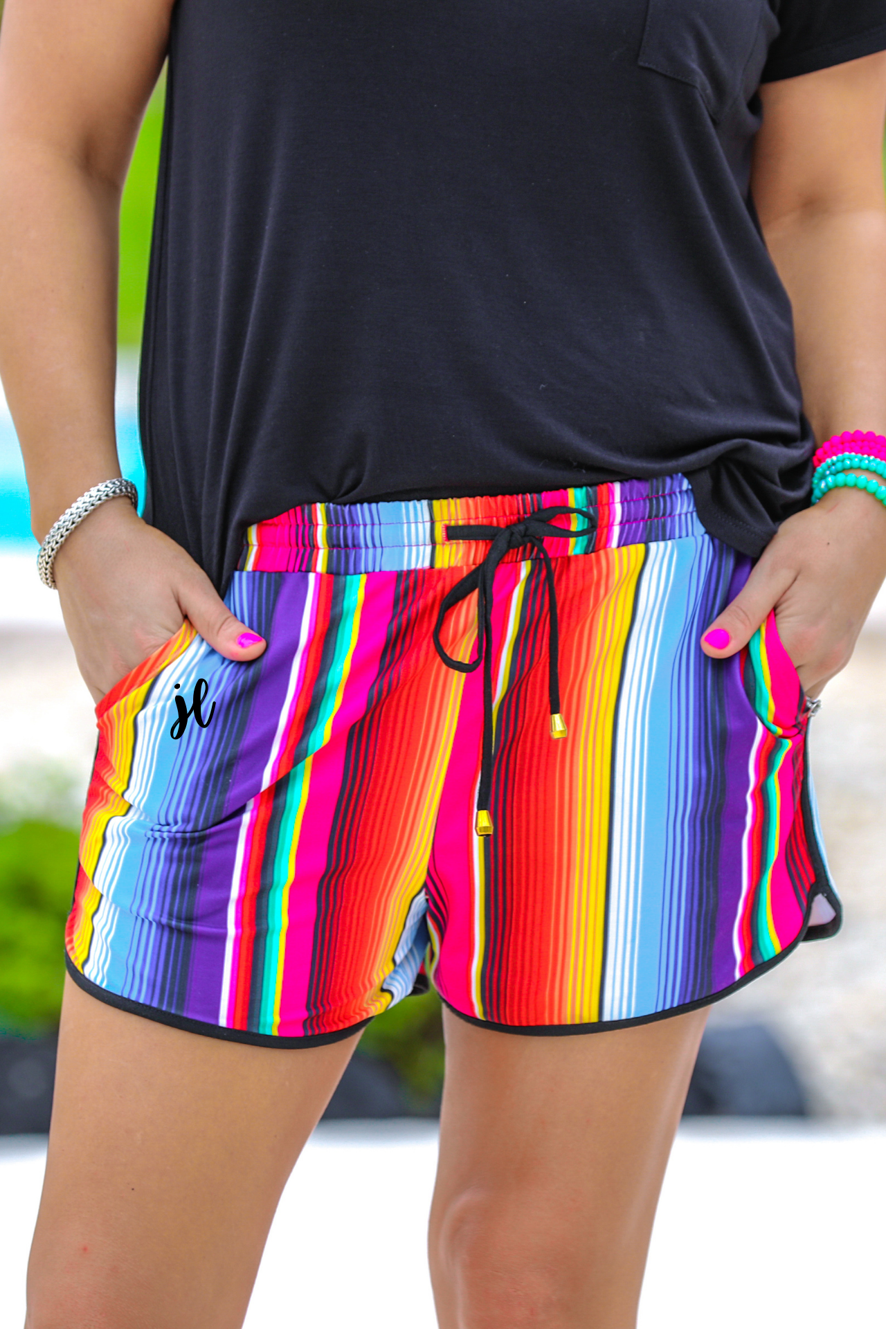 mid-rise relaxed fit activewear shorts with side pockets and a tie waist drawstring with gold bead accents, designed on a multicolor serape pattern print fabric and black trim