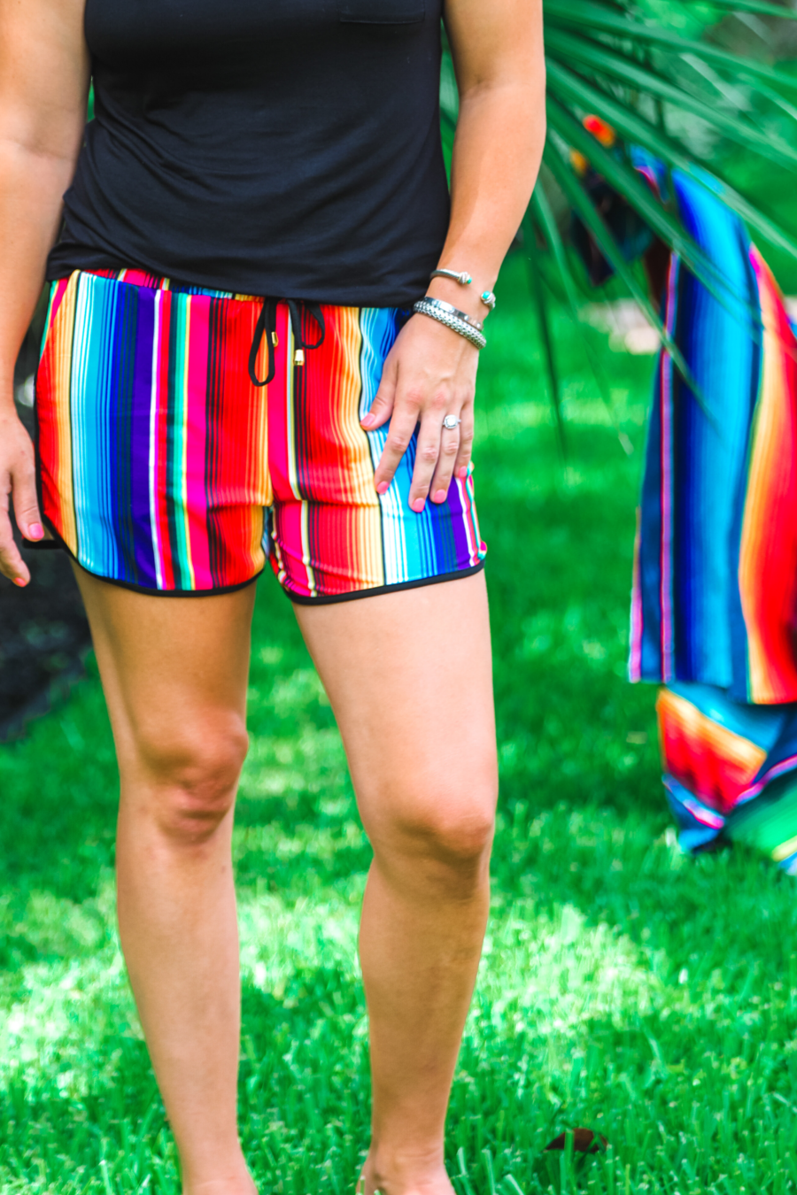 mid-rise relaxed fit activewear shorts with side pockets and a tie waist drawstring with gold bead accents, designed on a multicolor serape pattern print fabric and black trim